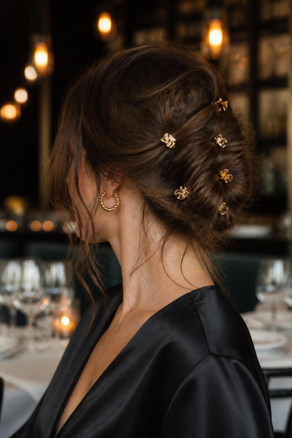Image Prompt:
A realistic editorial hairstyle photo of a woman with medium-length brunette hair styled into a loose low twist updo, several tiny gold mini claw clips scattered across the twist like a constellation, wispy strands around the face and nape, black satin top, softly lit restaurant background, warm indoor light, elegant creative hairstyle inspiration, high-resolution DSLR photography, no text, (no watermarks on images)