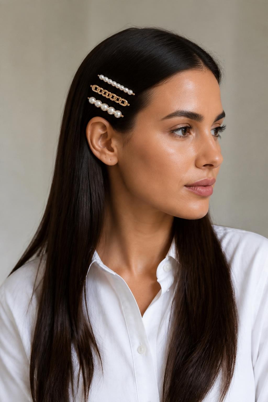 Image Prompt:
A realistic editorial beauty photo of a woman with long sleek dark brown straight hair styled with three slim French clips stacked neatly on one side above the ear, mixed pearl and gold clips, center part, glossy straight lengths, white tailored shirt, minimal studio background, soft neutral lighting, modern accessory-focused hairstyle inspiration, high-resolution DSLR photo, no text, (no watermarks on images)