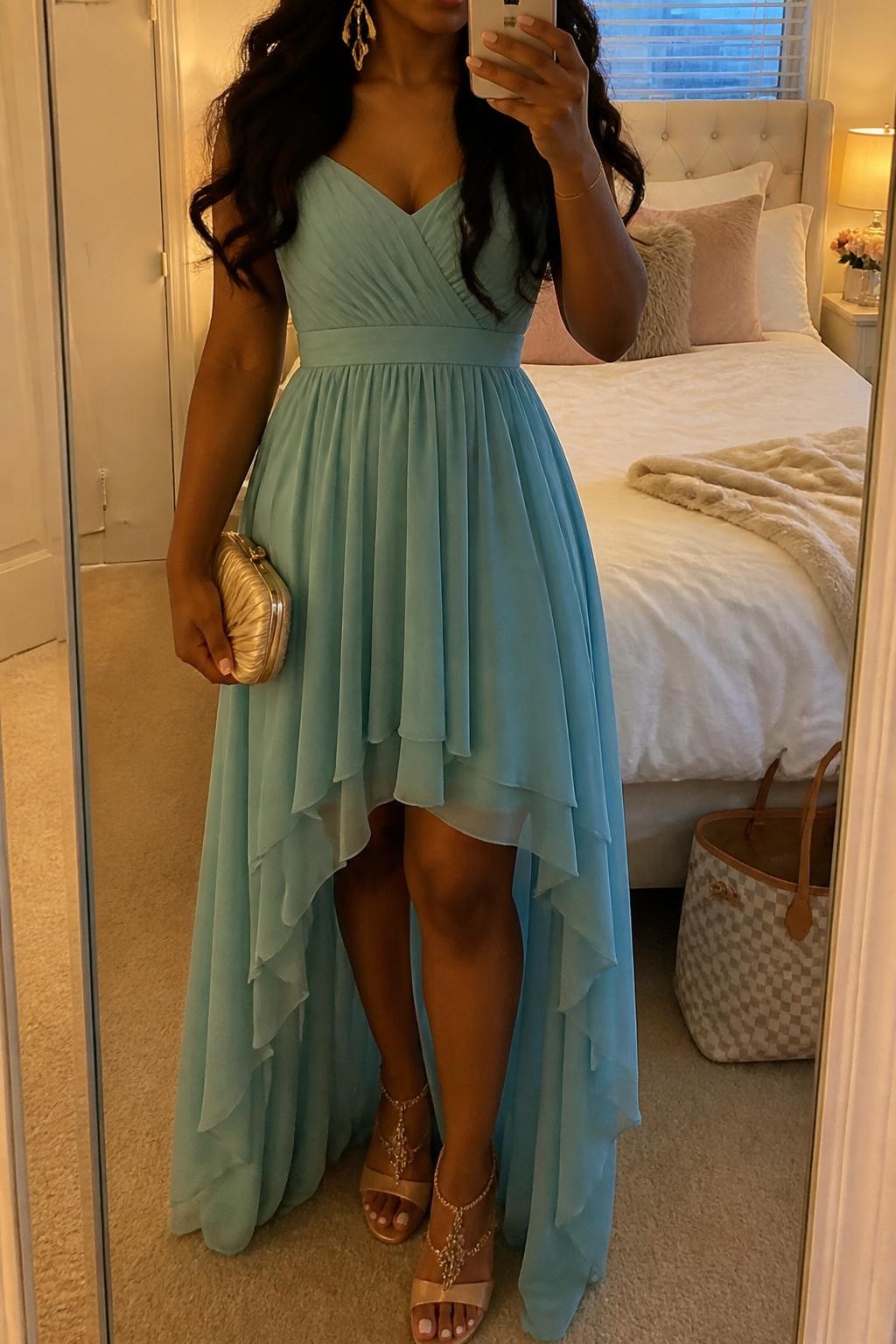 mirror selfie of a black woman wearing a soft teal chiffon high-low maxi dress with nude embellished heels, gold drop earrings, a satin small clutch, and loose curls hairstyle, holding a phone in front of a mirror, cropped at NECK so face doesn't show, with a natural casual selfie pose, in a feminine-themed bedroom, evening golden hour, including small lived-in details like soft bedding and a tote bag on the floor, latest iPhone photo quality (no watermarks on images)