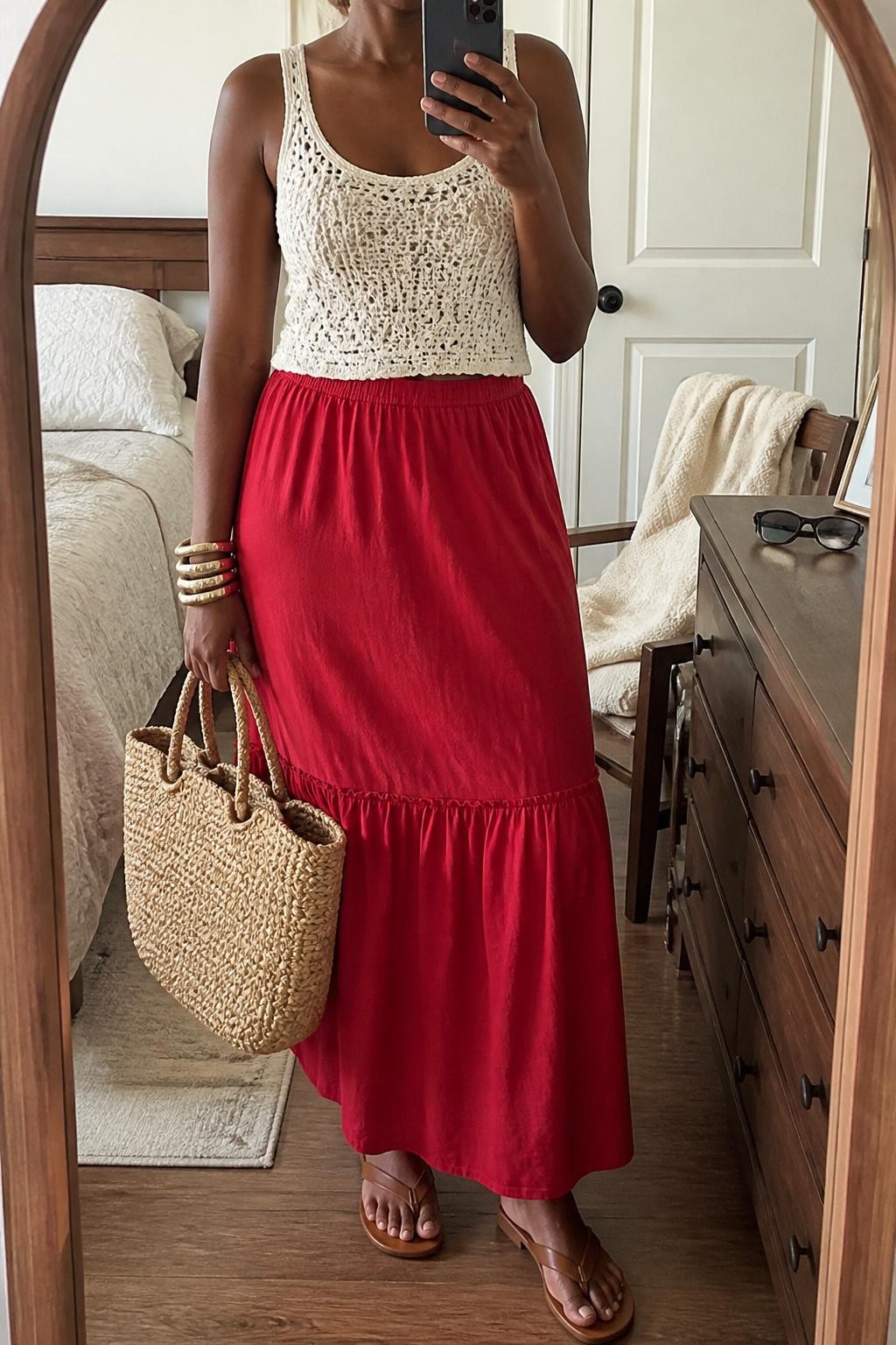 Outfit Image Prompt:
mirror selfie of a Black woman with dark brown skin wearing a white crochet tank top with a lined front, red cotton maxi skirt, tan flat sandals, a natural woven tote bag, and chunky gold bangles, clearly showing the exact clothing items and accessories listed, holding a phone in front of a mirror, cropped at NECK so the face does not show, relaxed casual selfie pose, in a cozy bedroom mirror setup, natural window light, with a folded blanket on a chair and sunglasses placed on a dresser, realistic casual latest iPhone photo quality, natural skin texture.