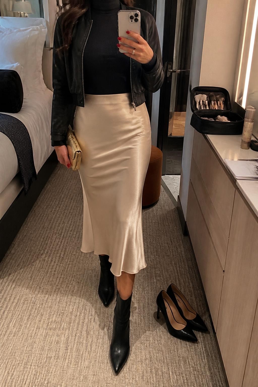 Outfit Image Prompt:
mirror selfie of a woman wearing a black fitted turtleneck top, champagne satin midi skirt, black ankle boots, a black cropped jacket, and a small gold clutch bag, holding a phone in front of a mirror, cropped at NECK so the face does not show, relaxed casual selfie pose, in a stylish cruise cabin mirror setup with warm moody lighting, including a pair of heels on the floor nearby and a makeup brush bag on the counter, natural skin texture, latest iPhone photo quality, realistic dinner outfit mirror selfie.
