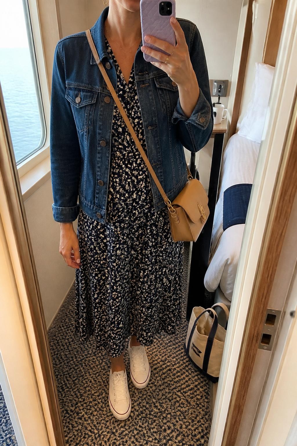 Outfit Image Prompt:
mirror selfie of a woman wearing a dark blue denim jacket, navy floral midi dress with small cream flowers, white low-top sneakers, a tan crossbody bag, and small gold hoop earrings, holding a phone in front of a mirror, cropped at NECK so the face does not show, relaxed casual selfie pose, in a cozy cruise cabin mirror setup with natural window light, including a coffee mug on a side table and a tote bag resting on the floor, natural skin texture, realistic latest iPhone photo quality.