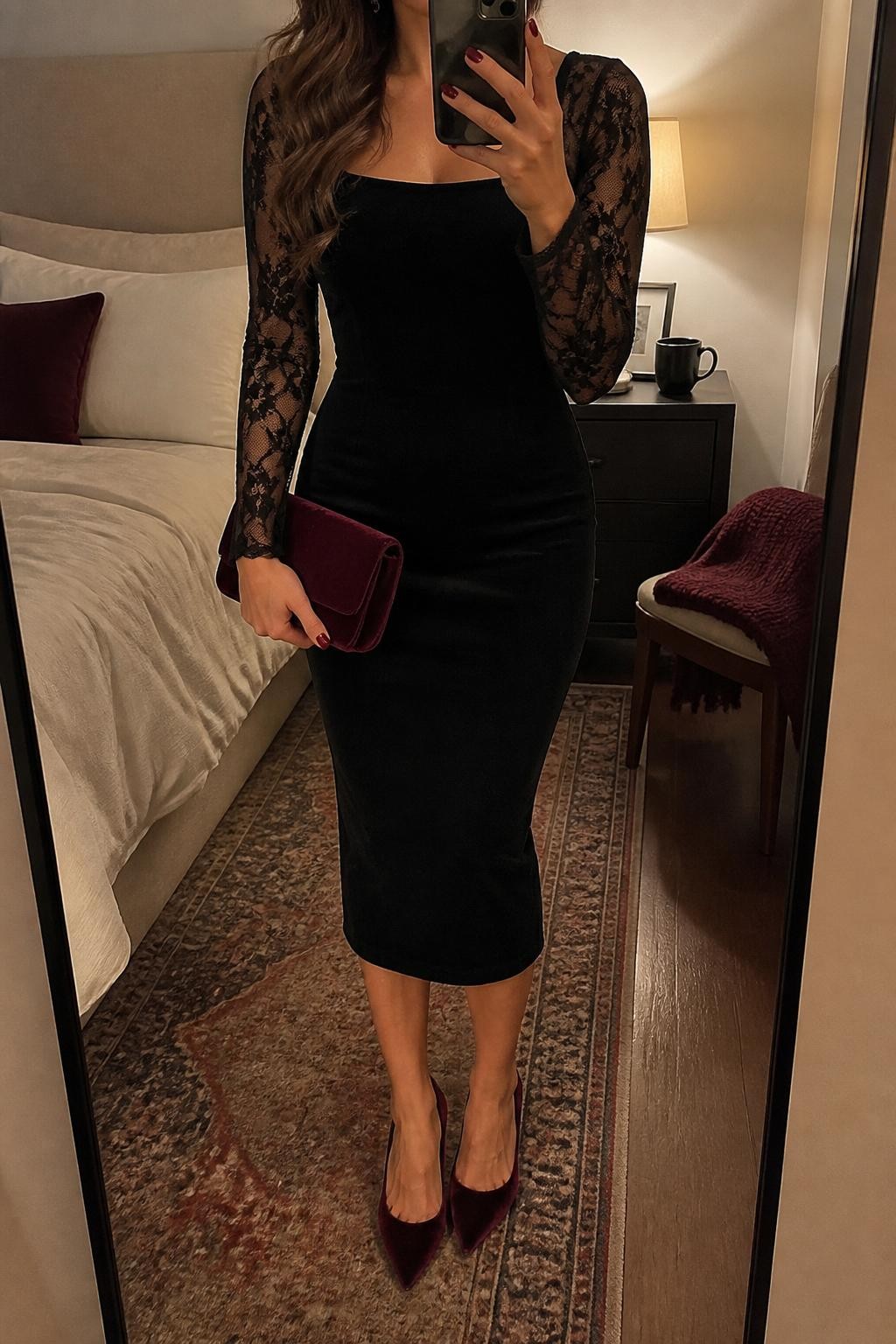 mirror selfie of a woman wearing a black fitted midi cocktail dress with sheer lace sleeves, burgundy velvet pointed-toe heels, small black crystal earrings, a burgundy velvet clutch, and soft waves with berry lipstick, clearly showing the same clothing items, colors, fabrics, and accessories listed in the Outfit Pieces section, holding a phone in front of a mirror, cropped at NECK so the face does not show, with a relaxed casual selfie pose, in a cozy bedroom mirror setup, warm moody lighting, including a coffee mug on a bedside table and folded blanket on a chair, latest iPhone photo quality.