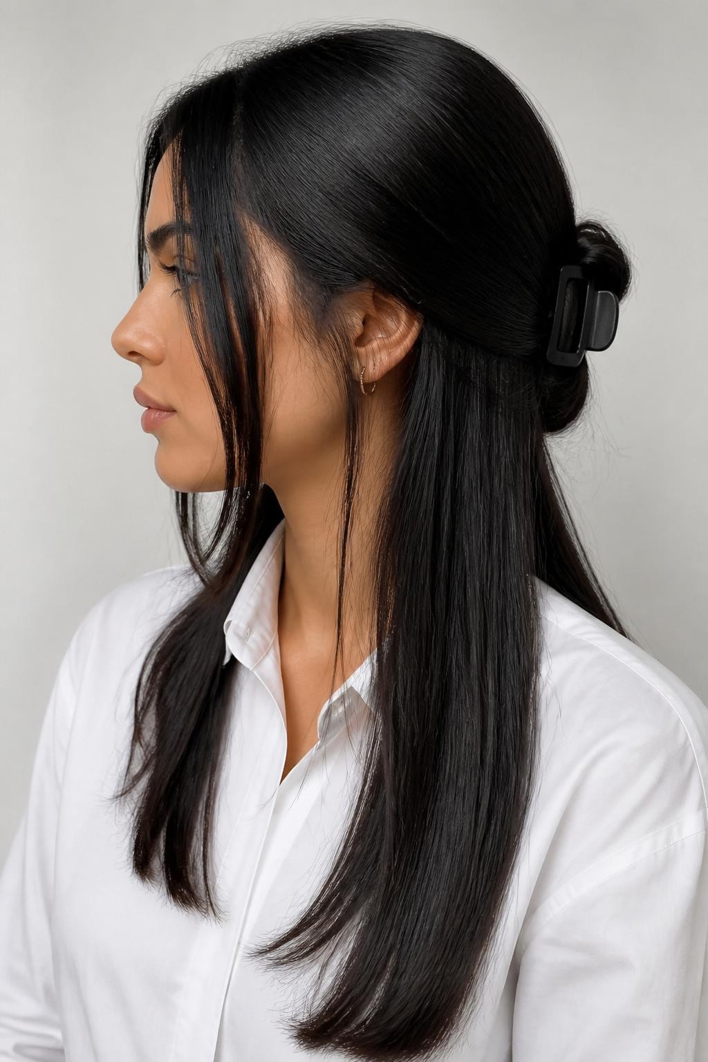 Image Prompt:
A realistic editorial hairstyle photo of a woman with long sleek black hair styled into a minimalist mid-height twist secured with a flat black claw clip, center part, glossy straight lengths with a few clean face-framing pieces, white tailored shirt, modern studio background, soft neutral lighting, polished minimalist hairstyle inspiration, high-resolution DSLR photo, no text, (no watermarks on images)