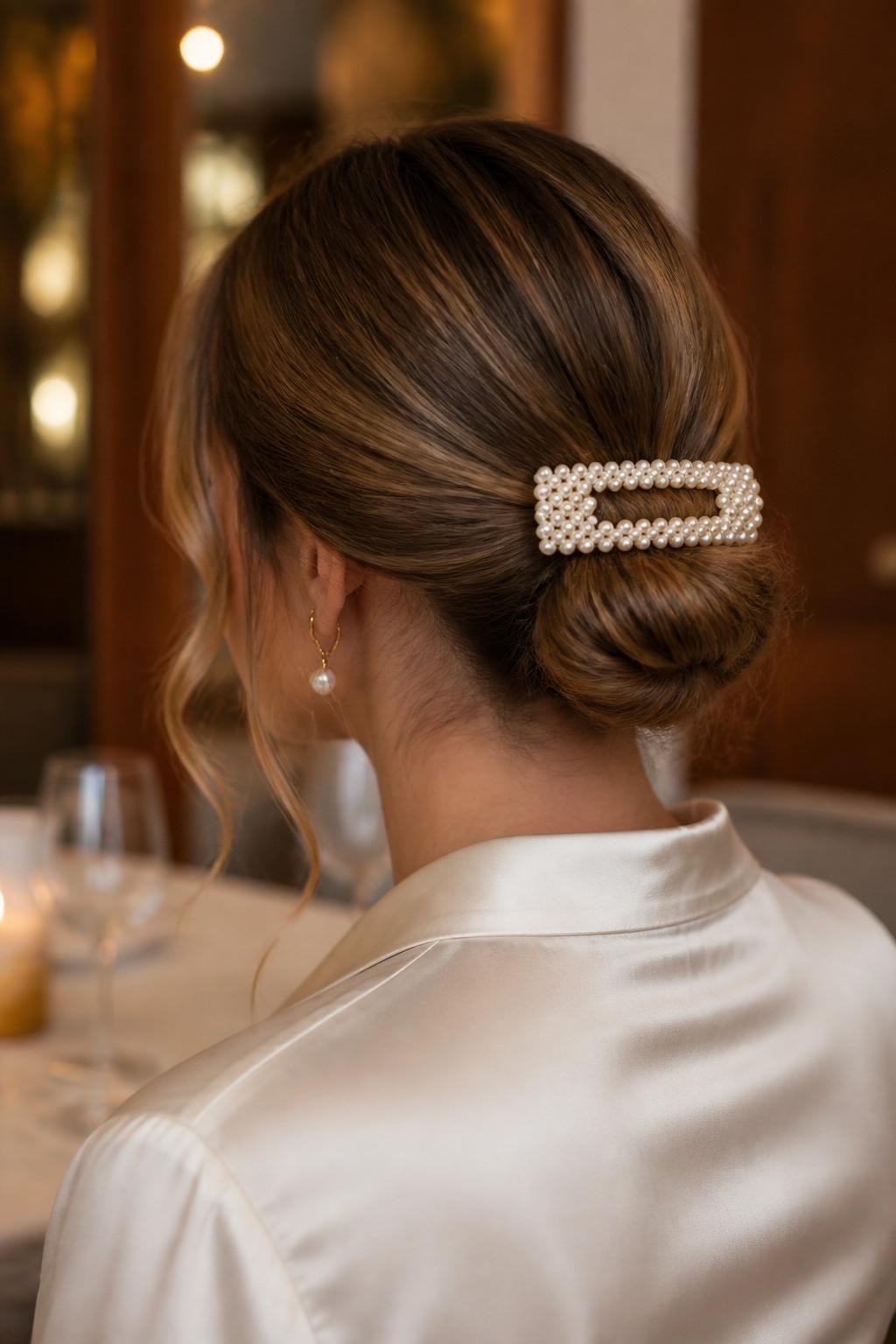 Image Prompt:
A realistic elegant hairstyle photo of a woman with medium-length dark blonde hair styled into a soft low bun, large rectangular pearl flat hair clip placed across the top of the bun, smooth crown, loose curled tendrils near the cheeks, satin ivory blouse, refined restaurant-style background, warm indoor lighting, polished feminine hairstyle inspiration, high-resolution DSLR photography, no text, (no watermarks on images)