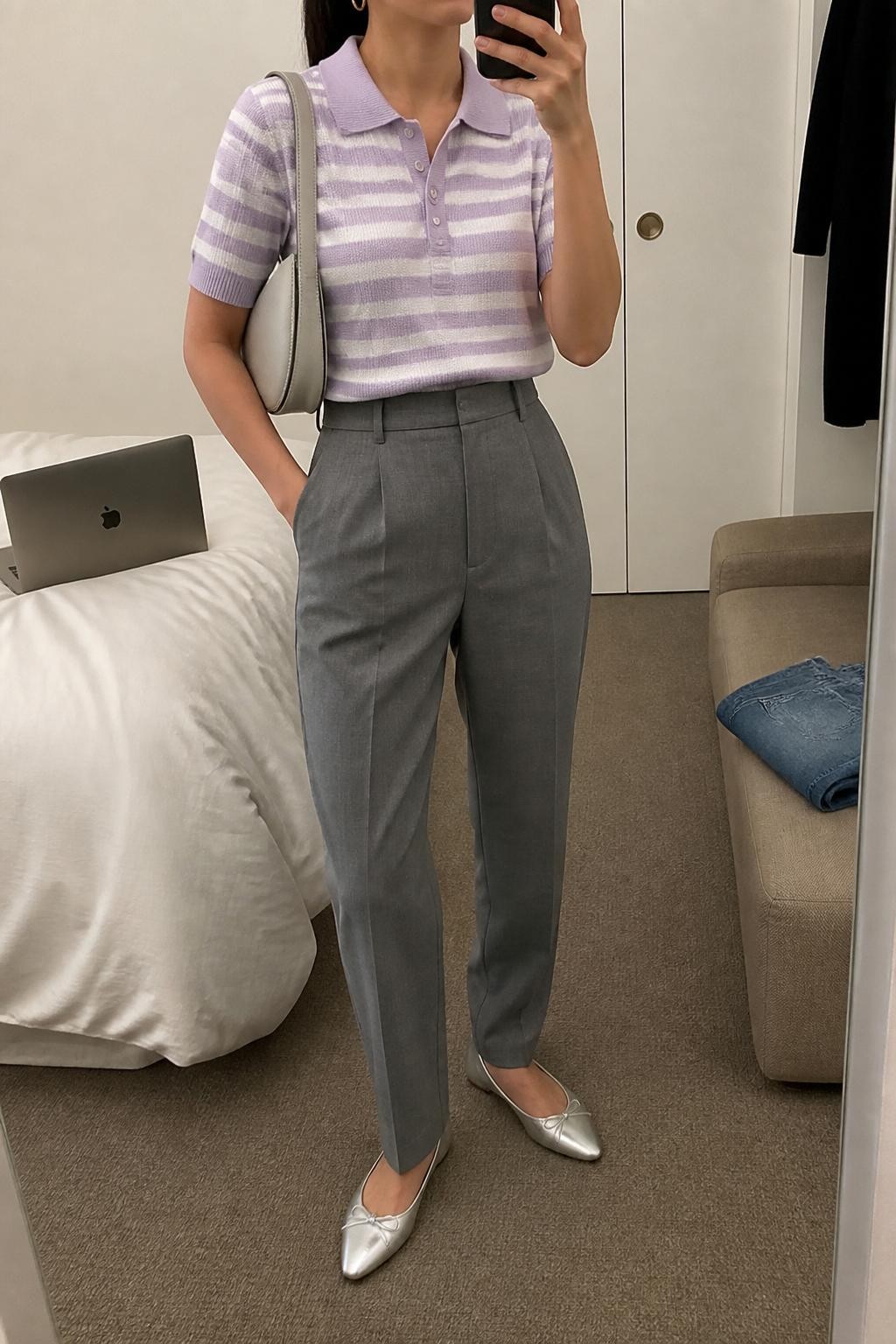mirror selfie of a woman wearing a lavender and white striped knit polo shirt tucked into gray high-waisted tailored trousers, silver pointed flats, pale gray crescent shoulder bag, and small silver huggie earrings, clearly showing the same clothing items, colors, fabrics, and accessories listed in the Outfit Pieces section, holding a phone in front of a mirror, cropped at NECK so the face does not show, with a relaxed casual selfie pose, in a minimal dressing room, soft indoor lighting, including a laptop on the bed and folded denim jeans on a bench, latest iPhone photo quality.
