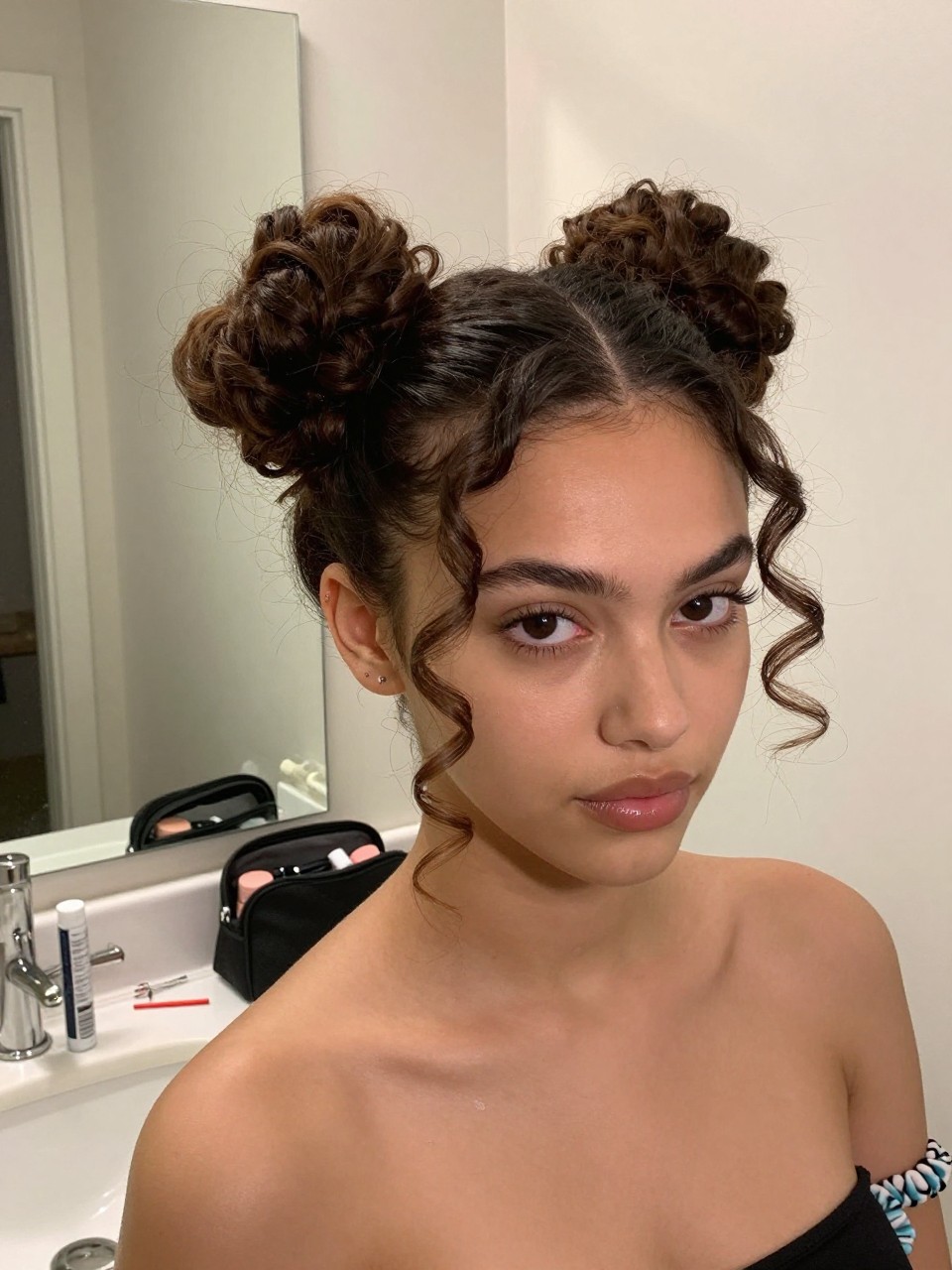 Image prompt

Photo of a woman wearing two soft 4A curly space buns with a clean middle part, loose coil ends around each bun, and two defined tendrils framing the face, front three-quarter view beside a bathroom vanity mirror, soft indoor lighting, containing a small lived-in detail such as bobby pins and curl gel on the counter, a makeup bag nearby, and two spare scrunchies on her wrist, realistic getting-ready moment, latest iPhone photo quality.