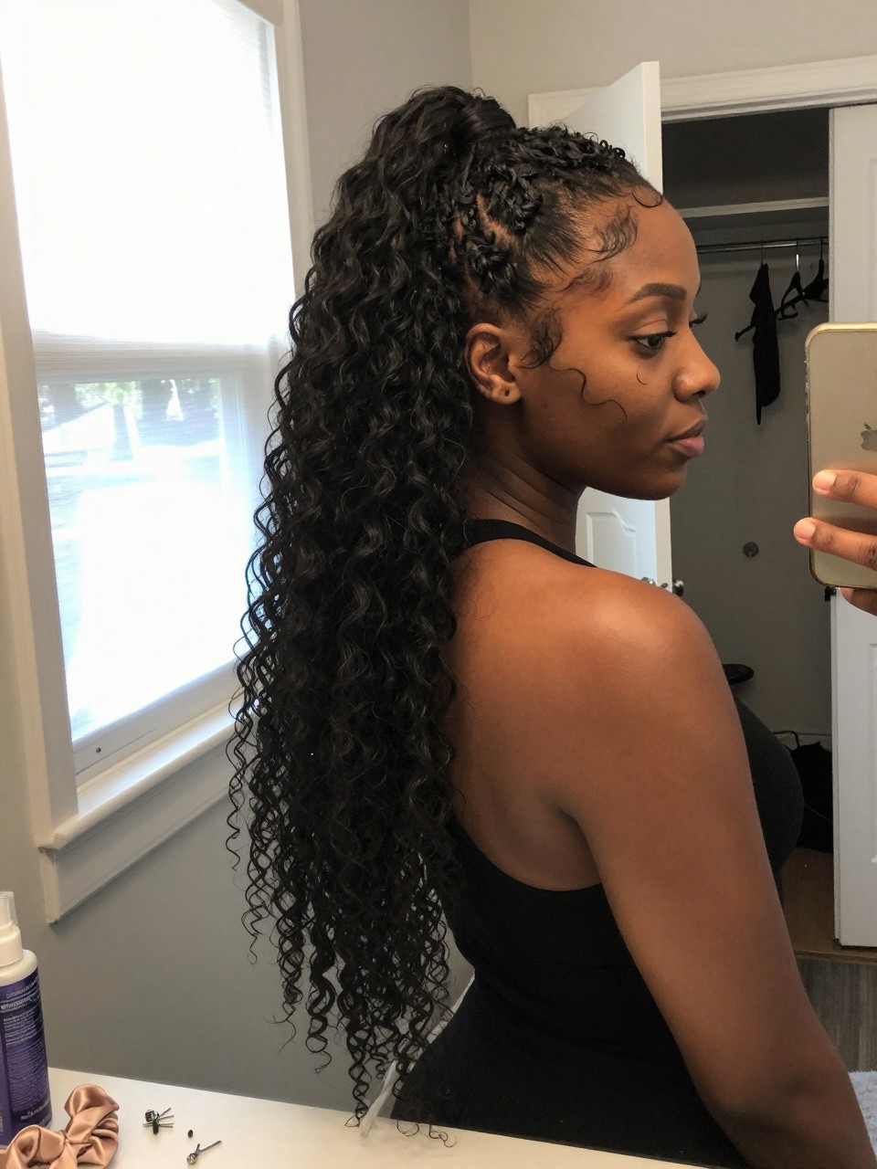 Image prompt
Photo of a Black woman wearing a long curly sew-in in a high half-up ponytail with a softly lifted crown, full loose curls falling down her back, and two defined face-framing pieces, candid bedroom mirror selfie, natural window light, containing a small lived-in detail such as bobby pins and a silk scrunchie on the dresser, a curl refresher bottle nearby, and a slightly open closet behind her, realistic getting-ready moment, latest iPhone photo quality.