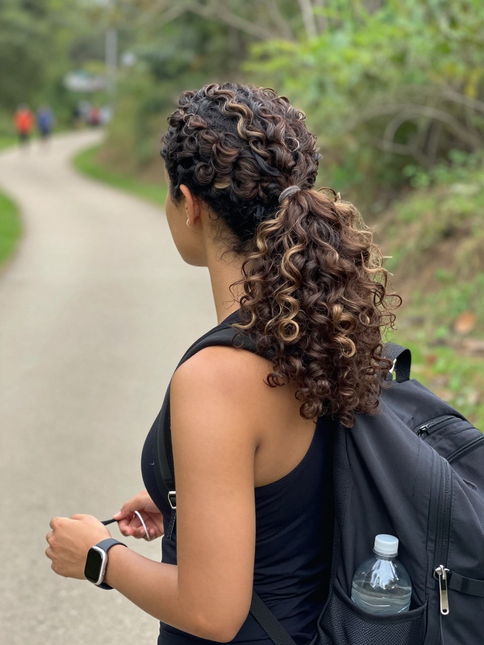 Image prompt
Photo of a woman wearing a low curly bubble ponytail with three compact rounded sections and a clean side part, back three-quarter view beside a softly blurred outdoor walking trail, natural daylight, containing a small lived-in detail such as a fitness tracker on her wrist, a water bottle in the side pocket of a backpack, and a spare elastic around her fingers, realistic candid active-day photograph, latest iPhone photo quality.
