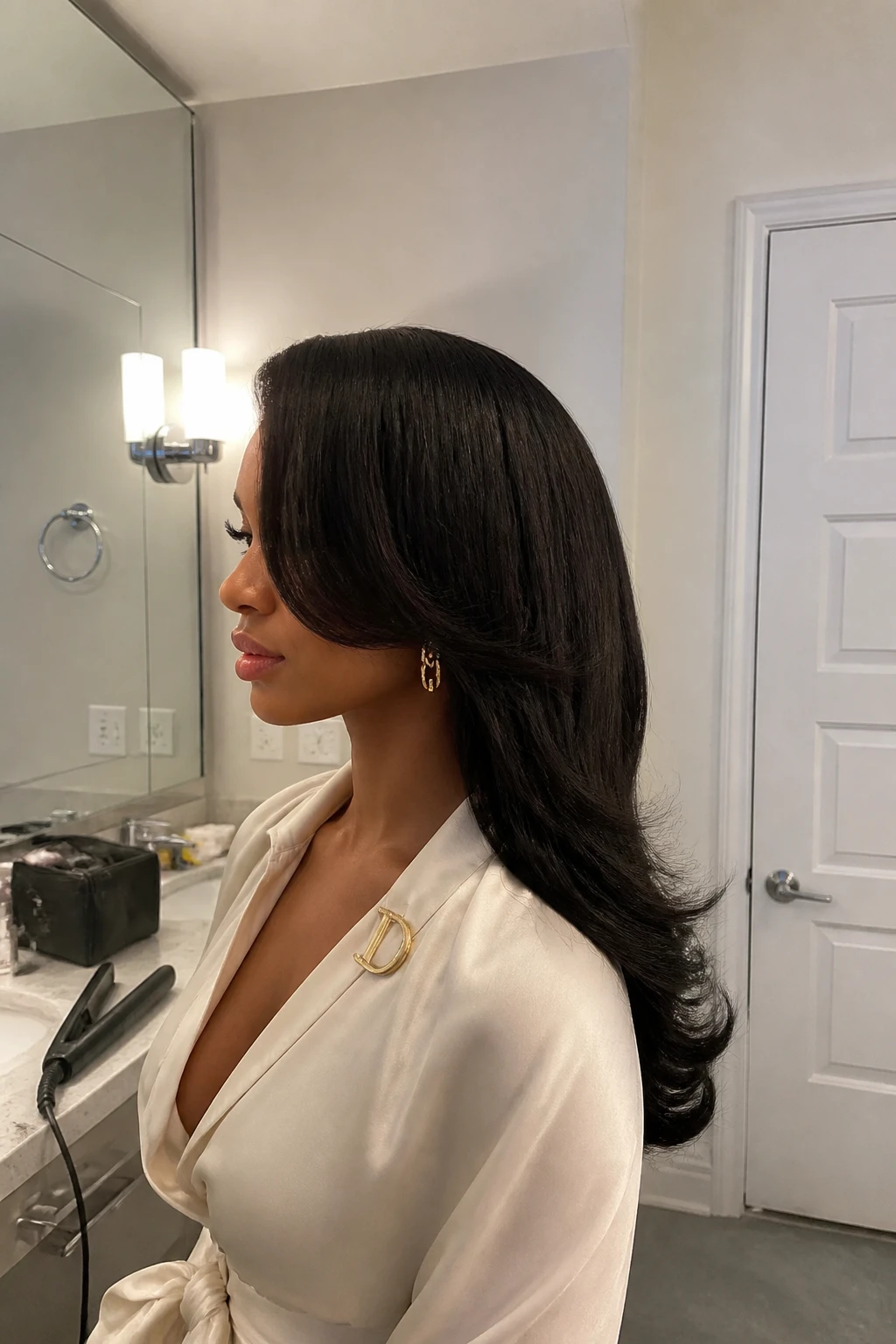 Image prompt

Photo of a woman wearing a deep side-part layered straight weave with smooth face-framing pieces and softly curved ends, side profile view highlighting the layers, standing beside a bathroom vanity mirror with a makeup bag and flat iron on the counter, soft indoor lighting, containing a small lived-in detail such as a gold hair clip attached to her blouse collar and statement earrings peeking through, realistic getting-ready moment, latest iPhone photo quality.