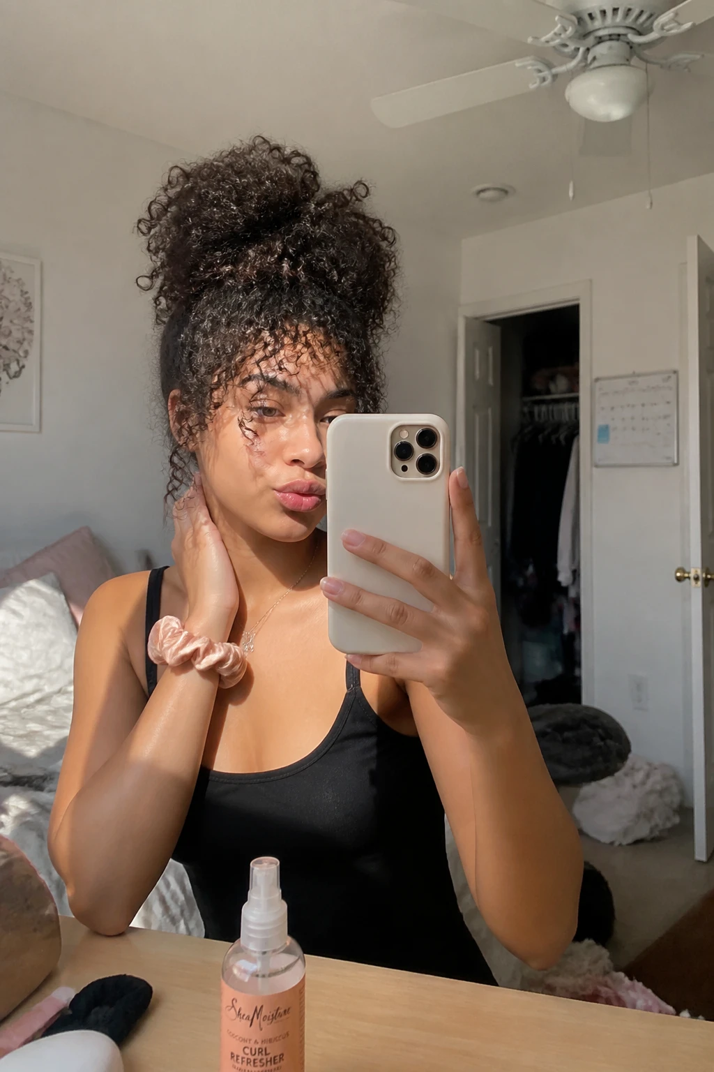 Image prompt

Photo of a woman wearing a high curly pineapple with full curls gathered loosely at the crown and soft curly bangs left around the forehead, candid mirror selfie in a sun-drenched bedroom, natural window light, containing a small lived-in detail such as a curl refresher bottle on the dresser, a silk scrunchie on her wrist, and a slightly open closet behind her, realistic bad hair day getting-ready moment, latest iPhone photo quality.