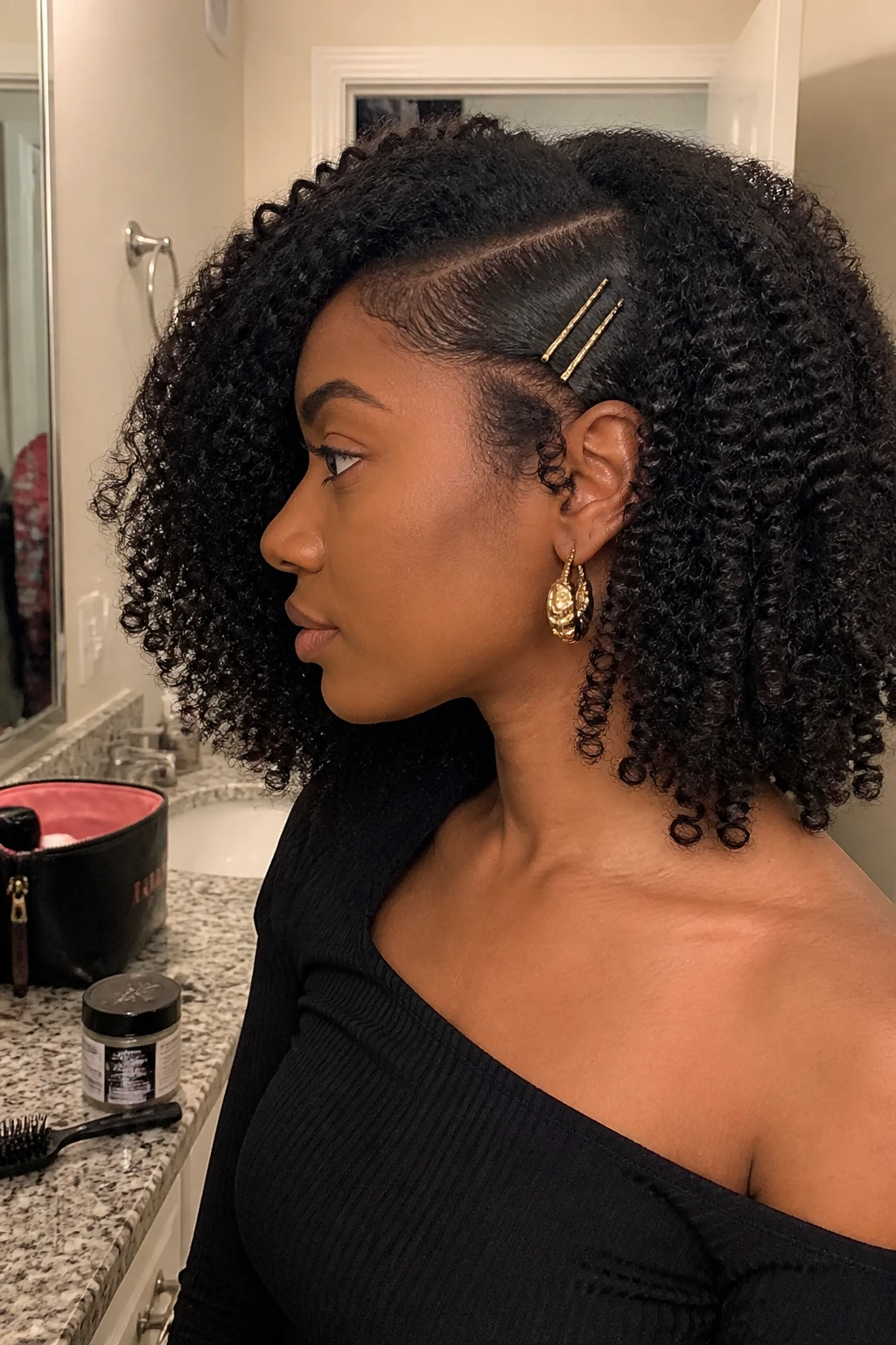 Image prompt

Photo of a woman wearing medium-length 4A curls with a deep side part, one side pinned neatly above the ear using two slim gold barrettes, and full defined coils sweeping across the opposite cheek, side profile view beside a bathroom vanity mirror, soft indoor lighting, containing a small lived-in detail such as edge gel and a small brush on the counter, a makeup bag nearby, and statement earrings peeking through, realistic getting-ready moment, latest iPhone photo quality.