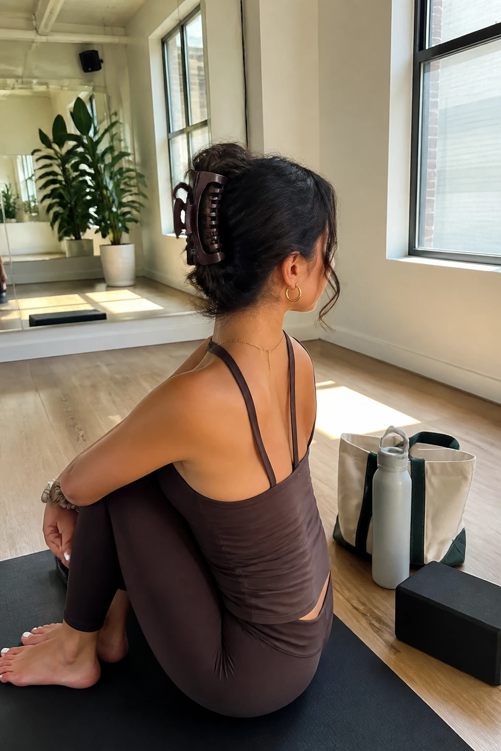 Image prompt
Photo of a Latina woman wearing a secure curly claw clip twist with the hair folded upward and soft curl ends tucked neatly over a large matte clip, back three-quarter view inside a sunlit yoga room, natural window light, containing a small lived-in detail such as a yoga block near a rolled mat, a water bottle beside a tote bag, and a silk scrunchie around her wrist, realistic pre-class moment, latest iPhone photo quality.