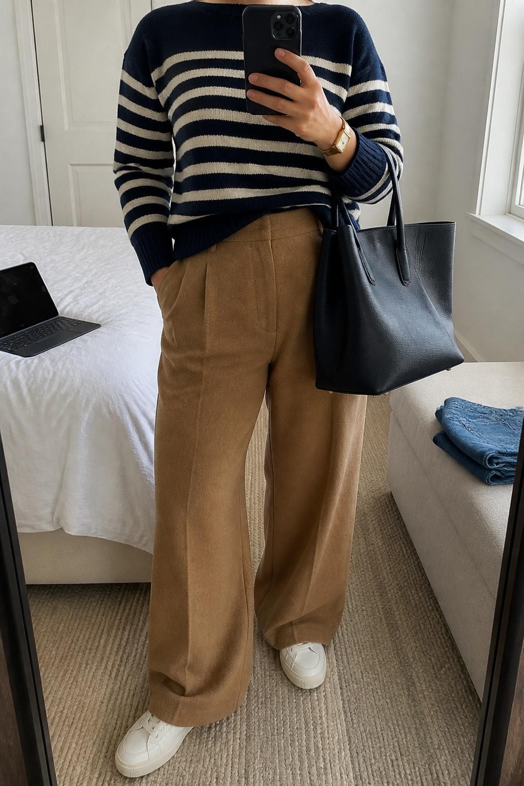 mirror selfie of a plus size woman wearing the exact outfit described above, a navy and cream striped knit sweater, camel wool-blend wide-leg trousers, low-profile white sneakers, navy leather structured tote bag, and simple gold watch, clearly showing the same clothing items, colors, fabrics, and accessories listed in the Outfit Pieces section, holding a phone in front of a mirror, cropped at NECK so the face does not show, with a relaxed casual selfie pose, in a minimal dressing room, natural window light, including a laptop or tablet on the bed and folded denim jeans on a bench, latest iPhone photo quality.