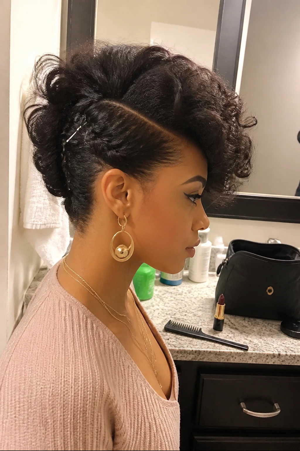 Image prompt
Photo of a woman wearing an asymmetrical curly faux hawk with a deep side part, one side pinned tightly upward with visible silver bobby pins, and full curls swept across the top, side profile view at a bathroom vanity mirror, soft indoor lighting, containing a small lived-in detail such as dark lipstick beside a makeup bag, a fine-tooth comb on the counter, and statement earrings peeking through, realistic getting-ready moment, latest iPhone photo quality.