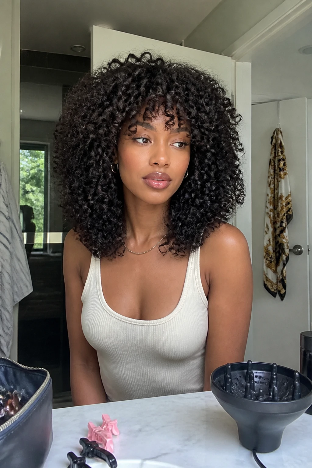 Image prompt

Photo of a woman wearing a shoulder-length 4A curly shag with short lifted crown layers, soft curly bangs, and longer dense coils around the shoulders, front three-quarter view in a softly lit bathroom mirror, natural window light, containing a small lived-in detail such as sectioning clips and a diffuser on the counter, a makeup bag nearby, and a silk scarf hanging from the door, realistic getting-ready moment, latest iPhone photo quality.