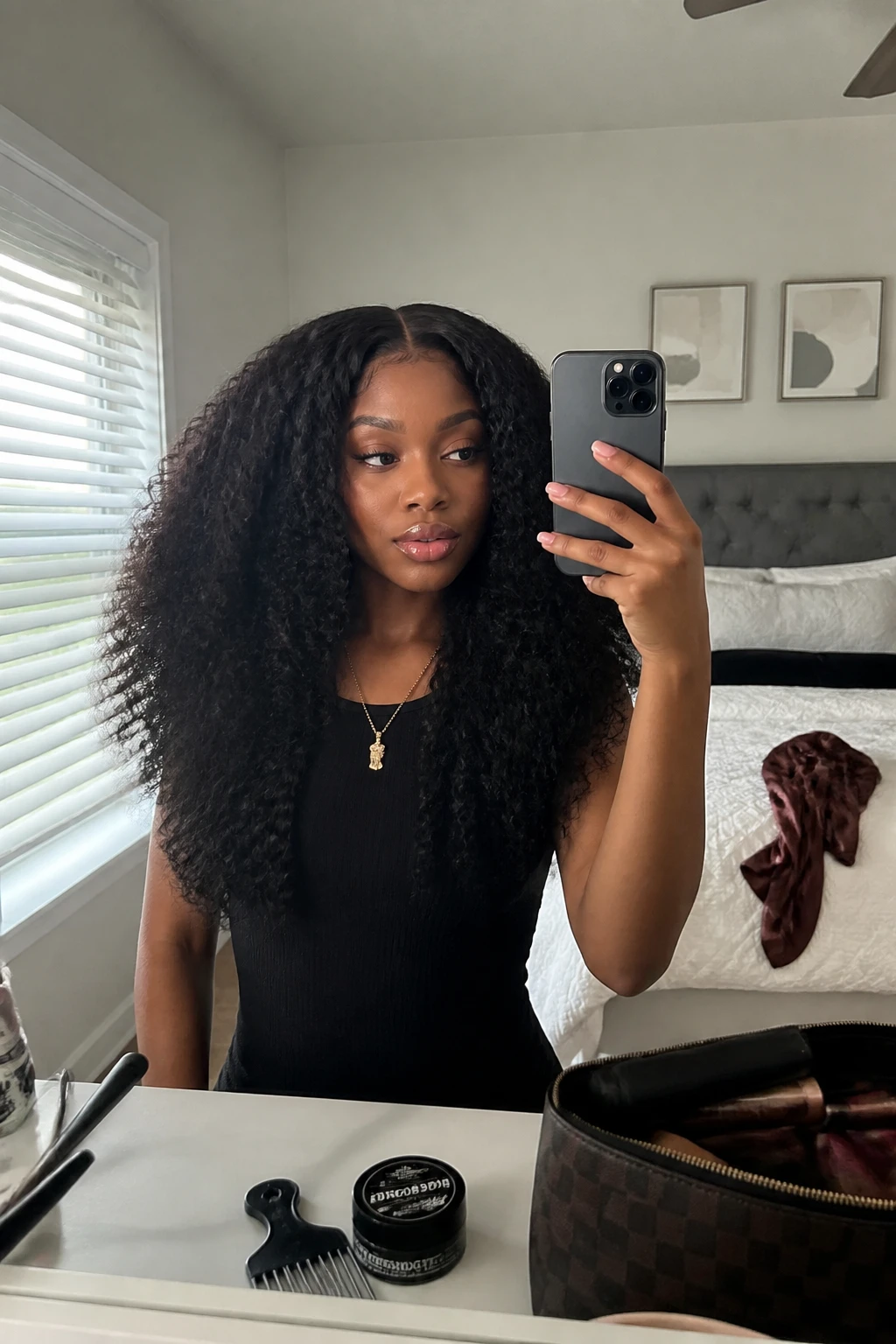 Image prompt
Photo of a Black woman wearing a full kinky curly sew-in with a clean middle part, dense natural-looking coils, soft volume around the crown, and subtle face-framing pieces, front-facing candid mirror selfie in a bright bedroom, natural window light, containing a small lived-in detail such as an afro pick on the dresser, edge gel near a makeup bag, and a satin scarf resting on the bed, realistic getting-ready moment, latest iPhone photo quality.