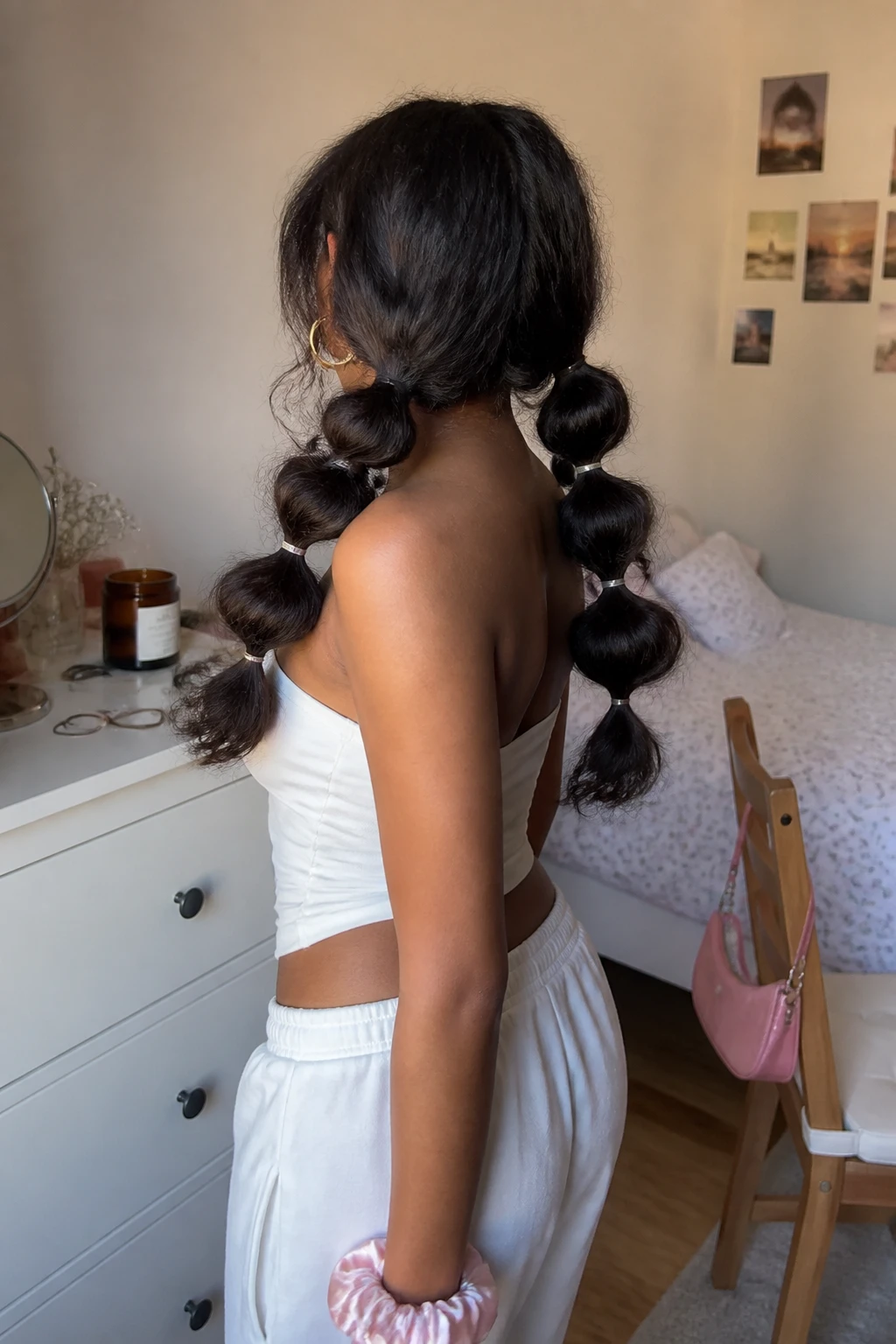 Image prompt
Photo of a South Asian woman wearing two low curly bubble pigtails with small clear elastics spaced evenly down each side, back three-quarter view highlighting the rounded sections and natural curl texture, standing in a softly lit bedroom, natural window light, containing a small lived-in detail such as extra elastics on the dresser, a tiny shoulder bag hanging from a chair, and a silk scrunchie on her wrist, realistic playful Y2K styling moment, latest iPhone photo quality.