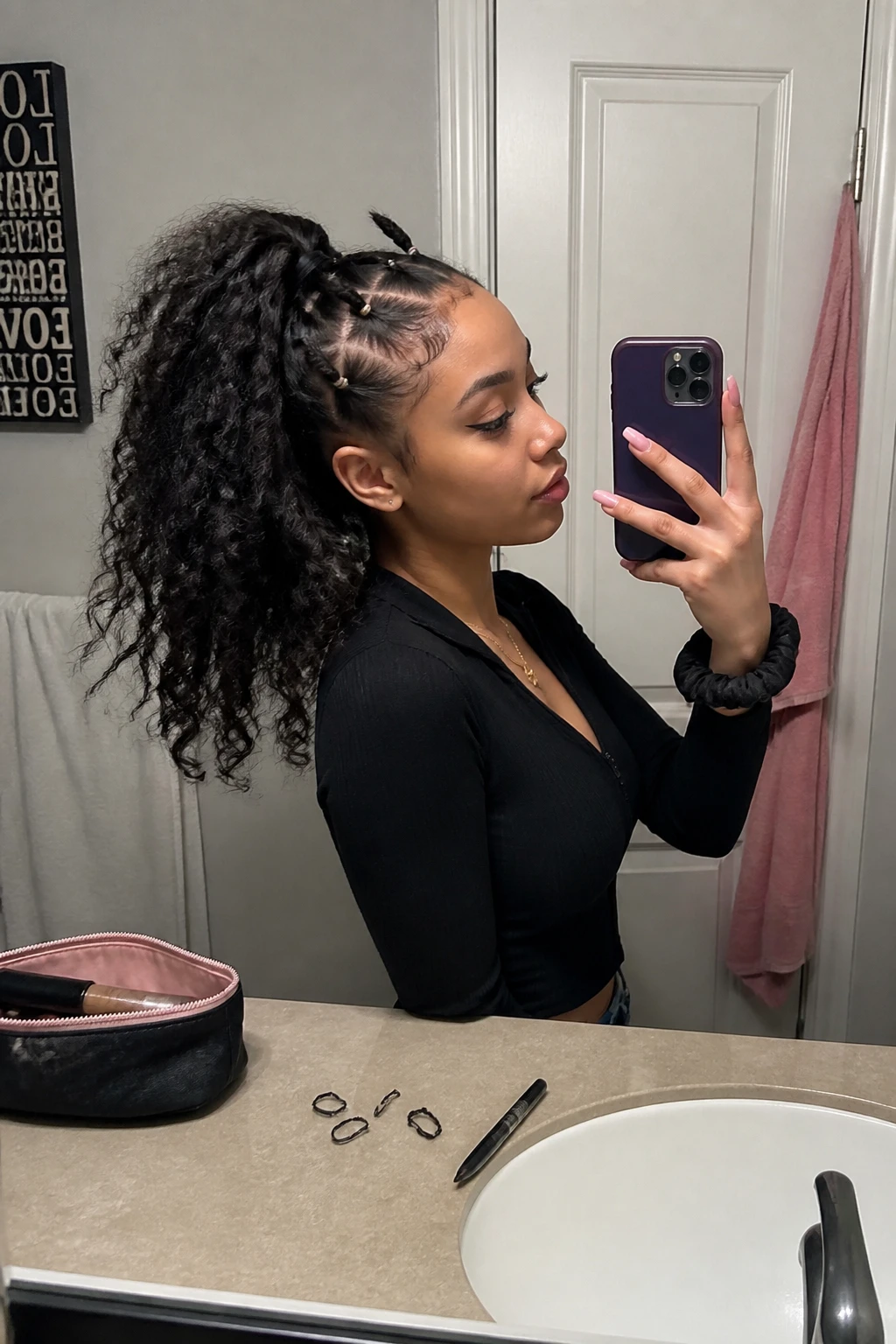 Image prompt
Photo of a woman wearing a high curly ponytail with several small twisted crown sections secured by black elastics, creating soft raised spikes before blending into the full ponytail, side profile view in a bathroom mirror, soft indoor lighting, containing a small lived-in detail such as tiny elastics on the counter, dark eyeliner beside an open makeup bag, and a black scrunchie on her wrist, realistic alternative getting-ready moment, latest iPhone photo quality.