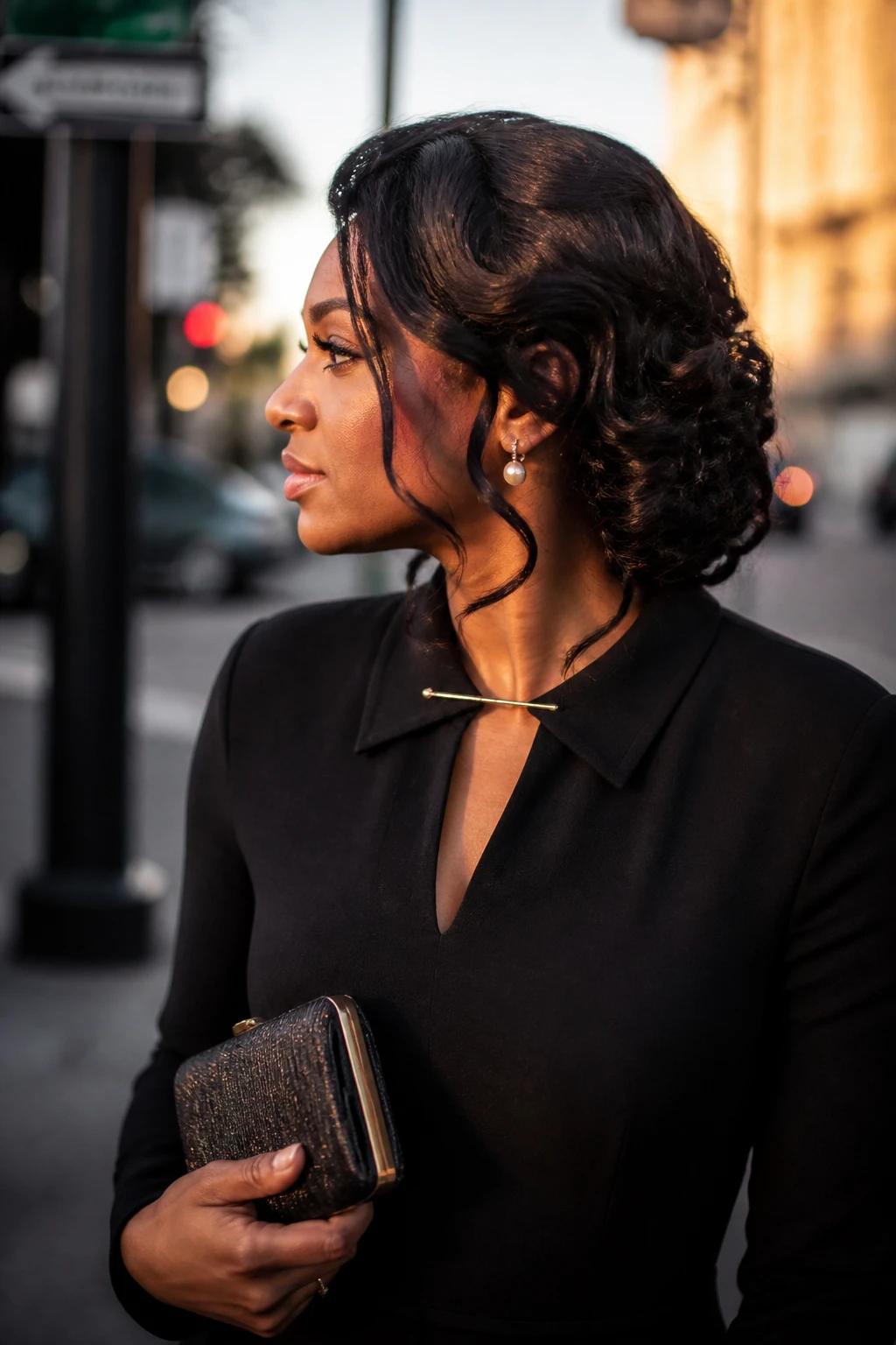 Image prompt
Photo of a Black woman wearing a side-swept curly sew-in updo with full curls pinned into a soft low shape behind one ear, gentle volume at the crown, and two face-framing tendrils, side profile view against a softly blurred city street background, golden hour glow, containing a small lived-in detail such as pearl earrings peeking through, a slim hair clip attached to her dress collar, and a small clutch held loosely in one hand, realistic candid photograph, latest iPhone photo quality.