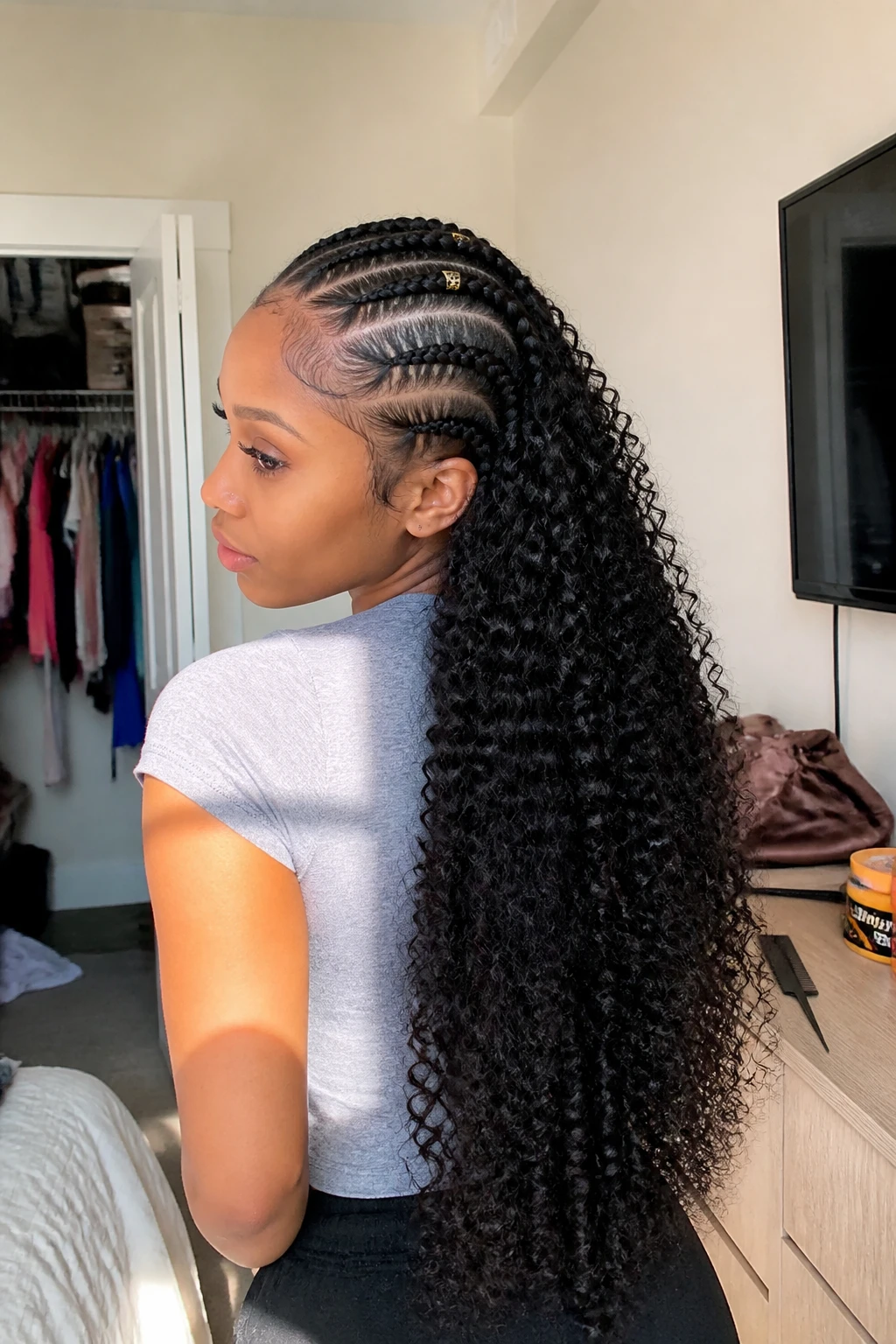 Image prompt
Photo of a Black woman wearing long curly sew-in hair with four neat front cornrows leading toward the crown, full springy curls flowing behind the braids, and small gold cuffs placed on two rows, back three-quarter view in a sun-drenched bedroom, natural window light, containing a small lived-in detail such as a rat-tail comb and edge gel on the dresser, a satin bonnet nearby, and a slightly open closet behind her, realistic getting-ready moment, latest iPhone photo quality.