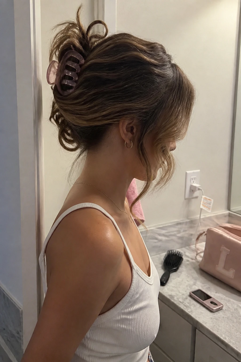 Image prompt
Photo of a woman wearing a curly claw clip updo with the hair twisted upward, soft curl ends spilling over the top, and two long face-framing pieces left loose, side profile view beside a bathroom vanity, soft indoor lighting, containing a small lived-in detail such as a translucent pink claw clip, a hairbrush near a makeup bag, and a flip phone-style case resting on the counter, realistic Y2K getting-ready moment, latest iPhone photo quality.