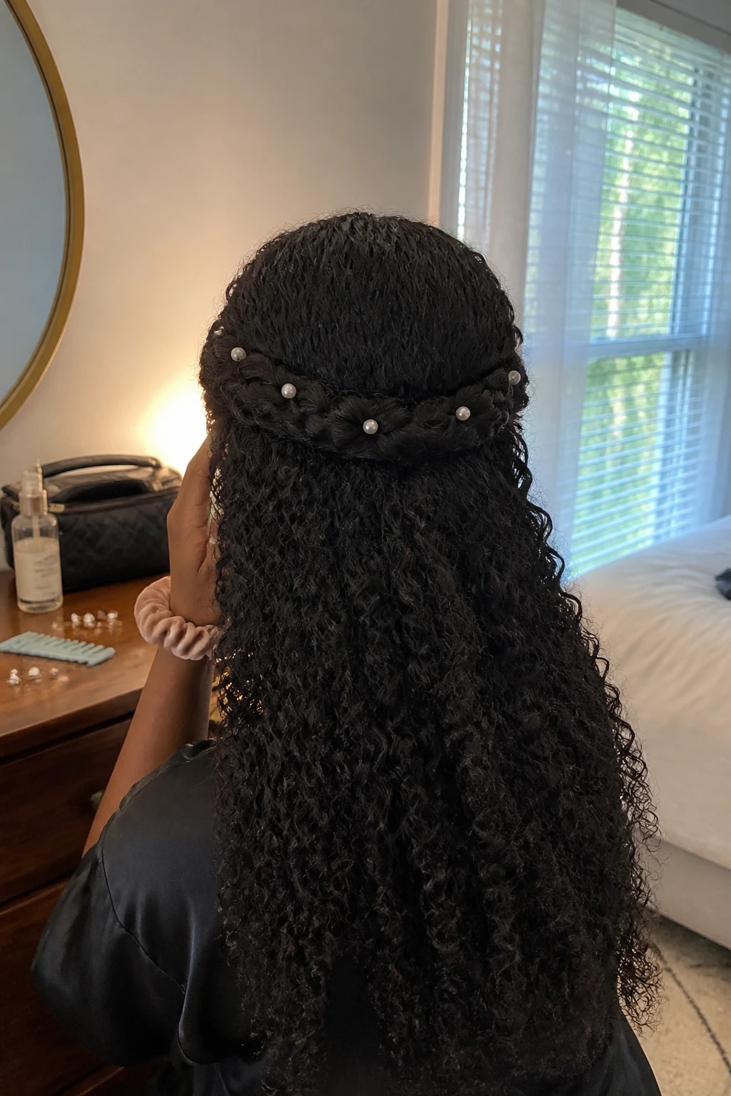 Image prompt
Photo of a Black woman wearing long 3B curls with two soft side braids crossed across the back like a crown, full defined ringlets flowing below, and small pearl pins tucked into the braids, back-of-head view in a softly lit bedroom, natural window light, containing a small lived-in detail such as extra pearl pins and a wide-tooth comb on the dresser, a makeup bag nearby, and a silk scrunchie on her wrist, realistic getting-ready moment, latest iPhone photo quality.