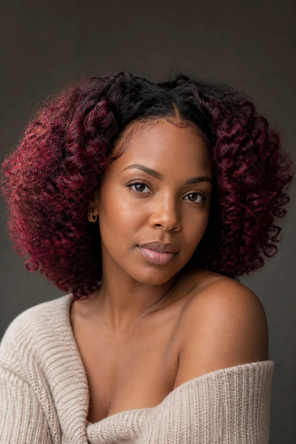 A realistic close-up portrait of a Black woman with warm medium-dark skin and rounded shoulder-length curls, soft black base with a cranberry velvet halo, deep cranberry-red color placed around the complete front hairline, temples, outer face-framing curls, and a narrow nape section, color shifting between garnet, raspberry-red, and muted wine under light, dark natural roots retained inside the halo, inner curls untouched, defined texture with natural frizz, cream off-shoulder sweater, small gold earrings, deep taupe background, soft window light, precise halo placement and realistic skin detail.