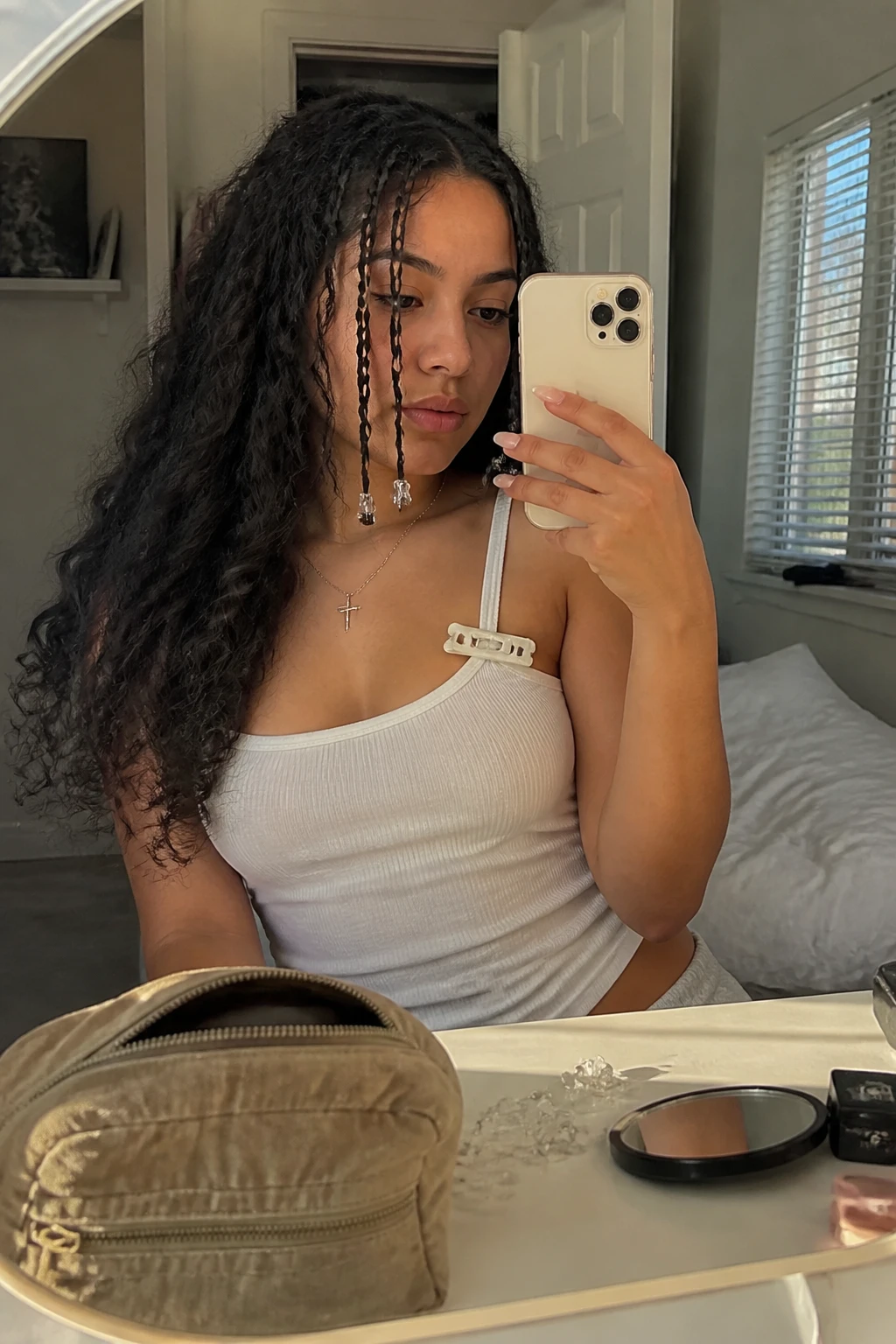 Image prompt
Photo of a Latina woman wearing long loose curly hair with four thin front mini braids, tiny clear elastics, and two small silver beads at the ends, candid mirror selfie in a sun-drenched bedroom, natural window light, containing a small lived-in detail such as clear elastics on the vanity, a compact mirror near a makeup bag, and a claw clip clipped to her tank top strap, realistic Y2K getting-ready moment, latest iPhone photo quality.