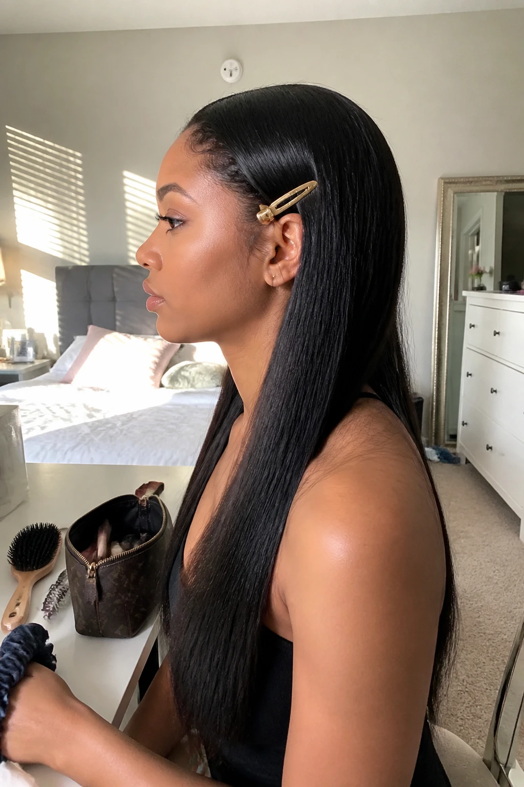 Image prompt

Photo of a woman wearing a long silky straight weave with one side pinned neatly behind the ear using a slim gold barrette, side profile view highlighting the accessory and smooth hair texture, standing in a sun-drenched bedroom, natural window light, containing a small lived-in detail such as a hairbrush on the vanity, a makeup bag nearby, and a silk scrunchie around her wrist, realistic getting-ready moment rather than staged hair photography, latest iPhone photo quality.